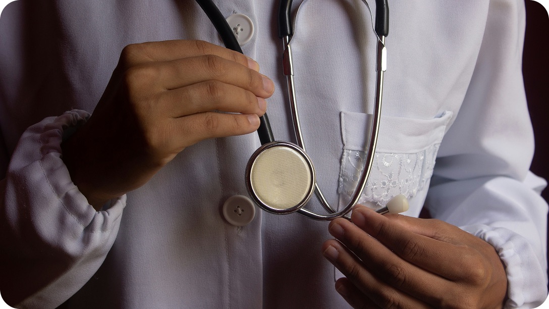 A doctor in a white coat holding the chest piece of a stethoscope